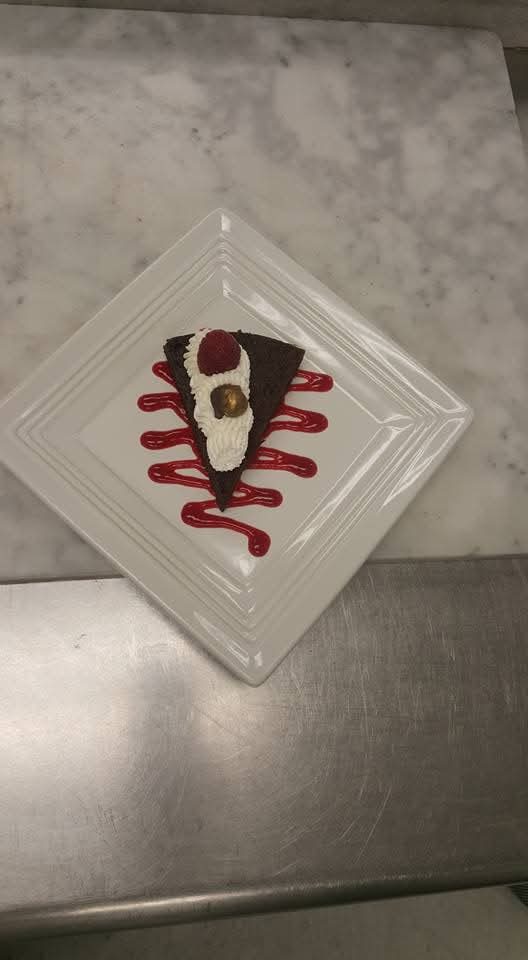 Slice of layered chocolate cake with raspberry sauce and a hazelnut