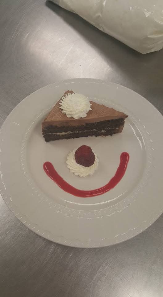 Slice of chocolate mousse cake plated with a smiling berry sauce design