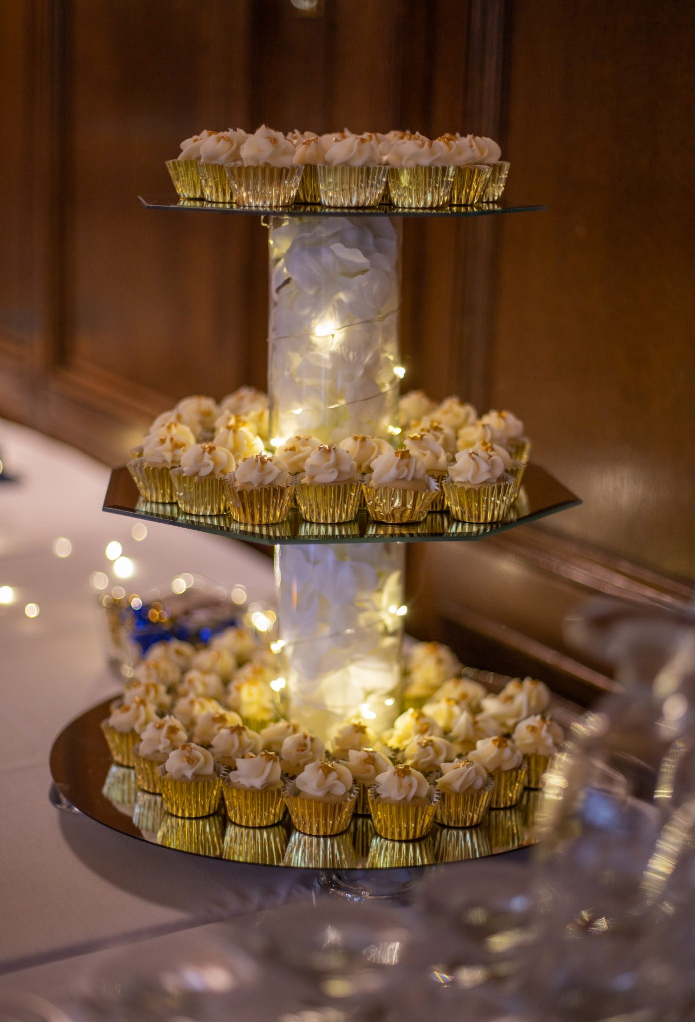 Tall gold cupcake tower with fairy-lit centerpiece