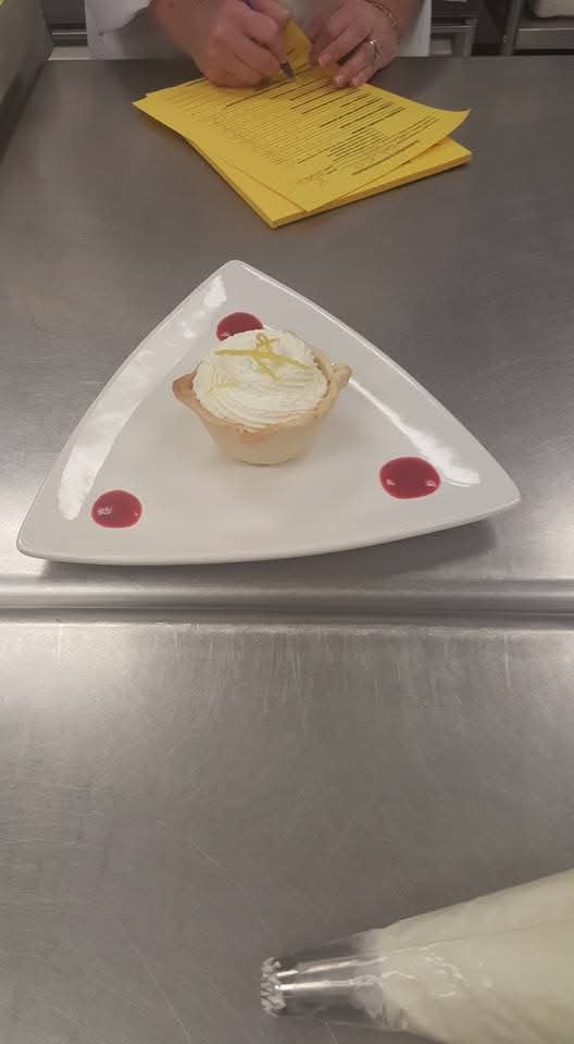 Individual lemon meringue tart with berry sauce on a triangular plate