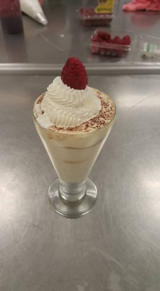 Layered tiramisu parfait in a glass with whipped cream and raspberry